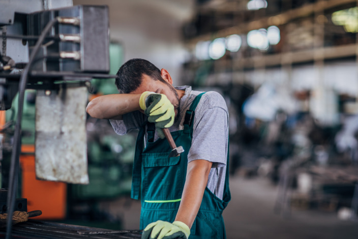 Handwerker steht in der Werkstatt und wischt sich den Schweiß von der Stirn