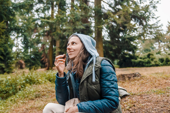 Frau macht im Wald beim Wandern eine Essenspause mit dem Proviant aus ihrem Rucksack.