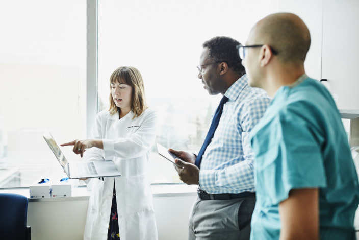 Drei Krankenhausmitarbeiter besprechen etwas am Laptop