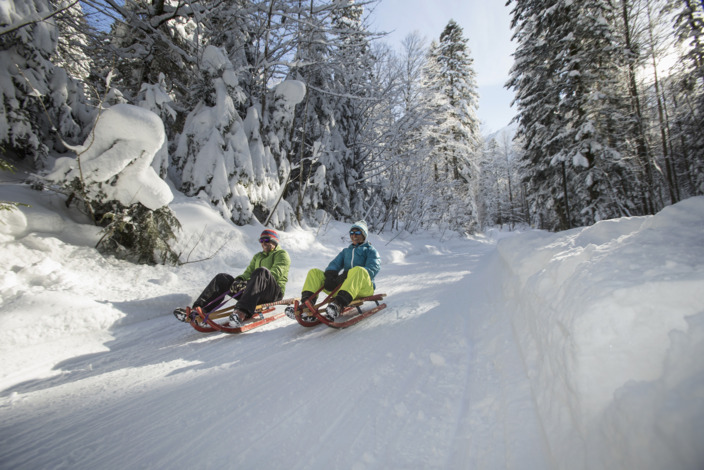 Zwei Personen auf Rodeln in verschneiter Winterlandschaft