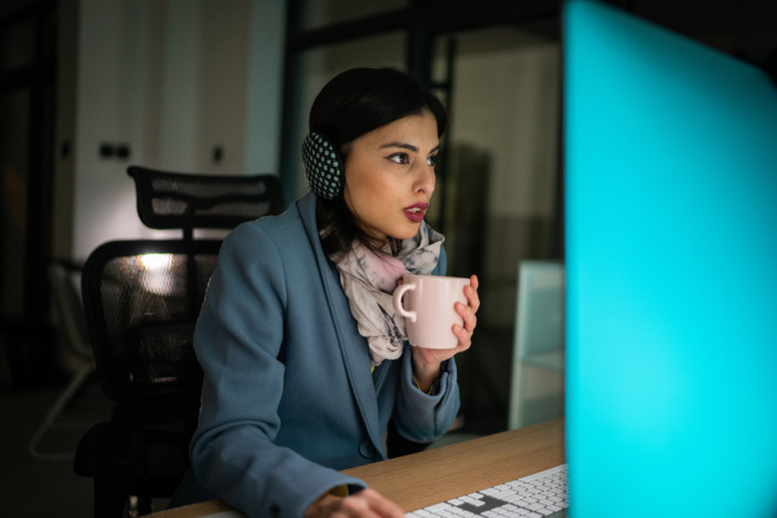 Frau trink fröstelnd am Arbeitsplatz einen Tee