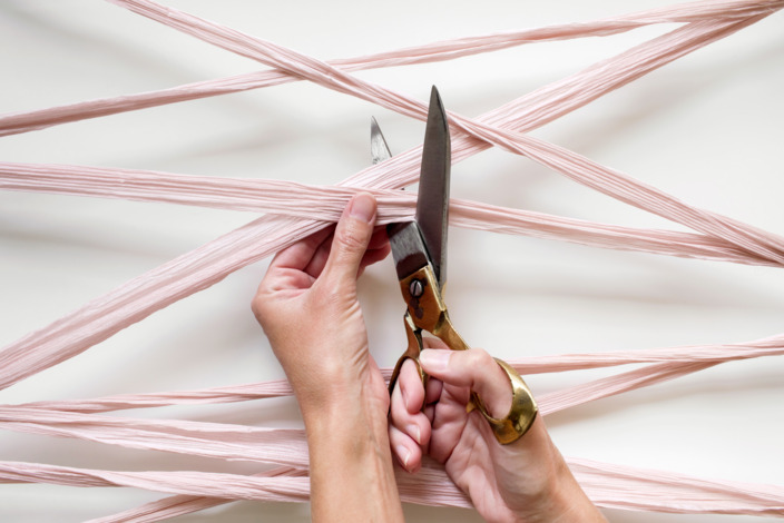 Schere in der Hand durchschneidet rosa Bänder