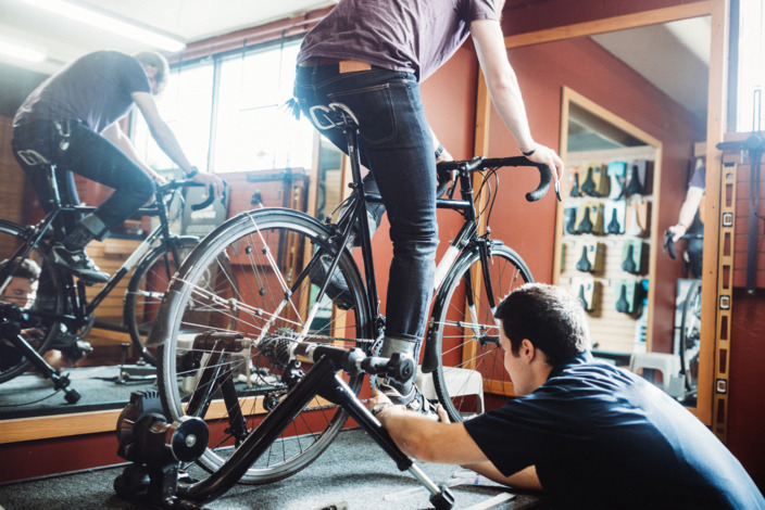 Mann sitzt auf einem Fahrrad, das Fahrrad ist in einem Gestell fixiert