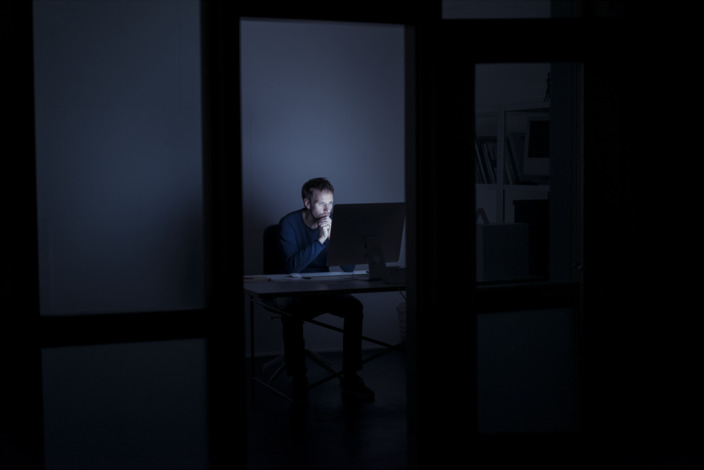 Mann sitzt im dunklen Büro vor dem PC