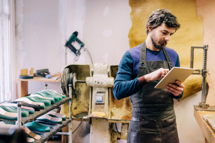 Handwerker steht in Werkstatt und arbeitet am Tablet