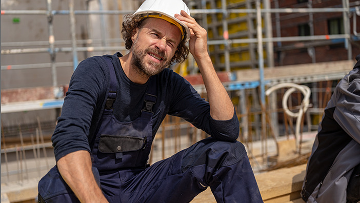 Mann mit Helm auf Baustelle schützt sich mit der Hand vor der Sonne.