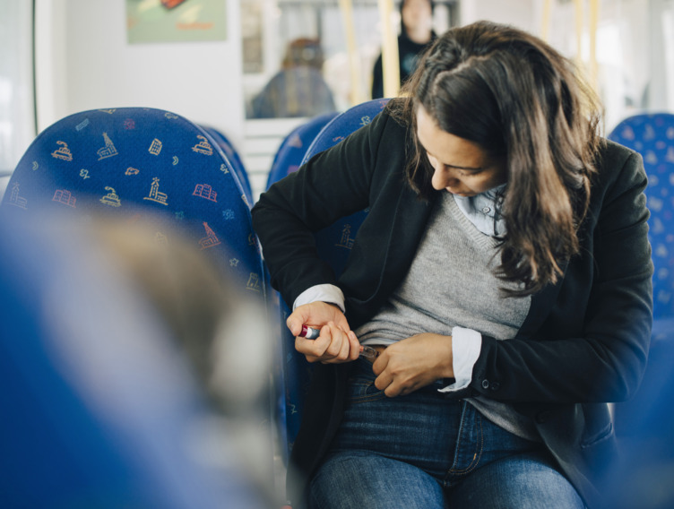 Frau sitzt in der Bahn und sticht sich mit einem Insulin-Pen