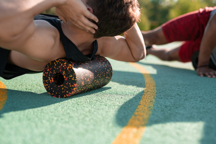 Mann in Sportkleidung rollt mit der Schulterpartie über die Faszienrolle