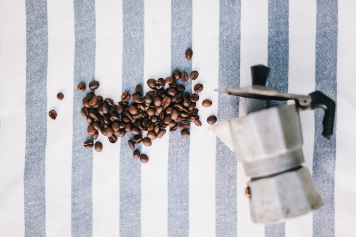 Espressokanne und Kaffeebohnen auf einer gestreiften Tischdecke.