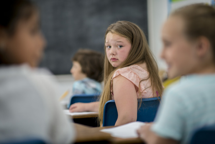 Schülerin die verängstigt ihre Schulkameraden in der Klasse anschaut.