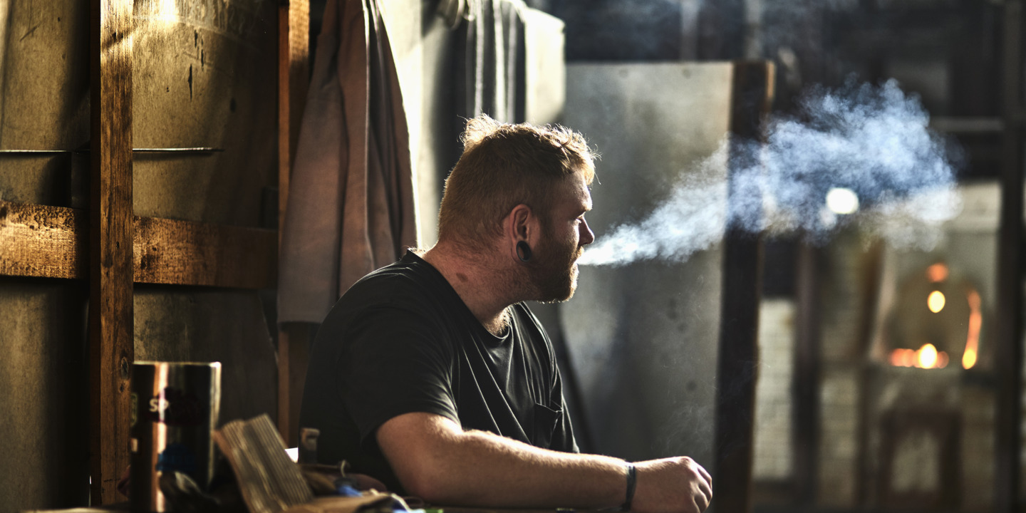 Ein Handwerker sitzt in der Werkstatt und raucht eine Zigarette. 