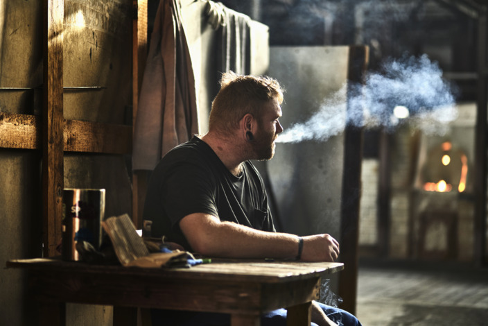 Ein Handwerker sitzt in der Werkstatt und raucht eine Zigarette. 