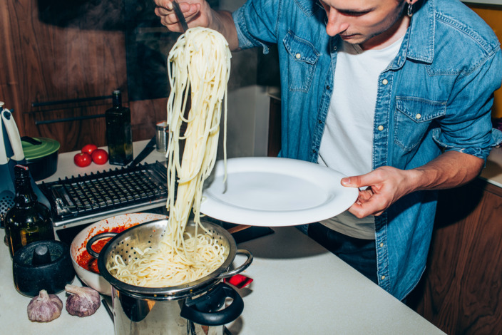 Student nimmt sich eine große Portion Spaghetti aus einem Kochtopf