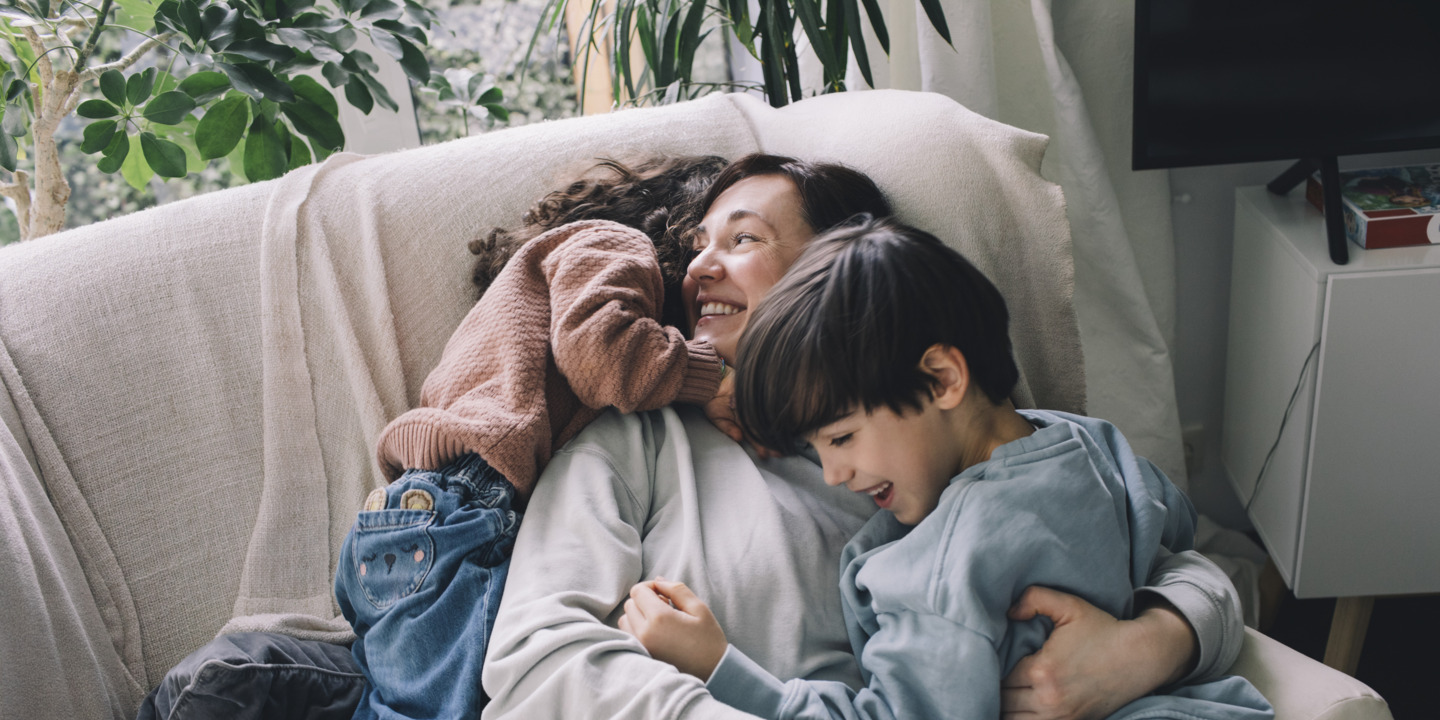 Eine Mama kuschelt mit ihren beiden Kindern auf dem Sofa. 