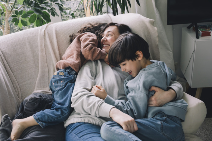 Eine Mama kuschelt mit ihren beiden Kindern auf dem Sofa. 