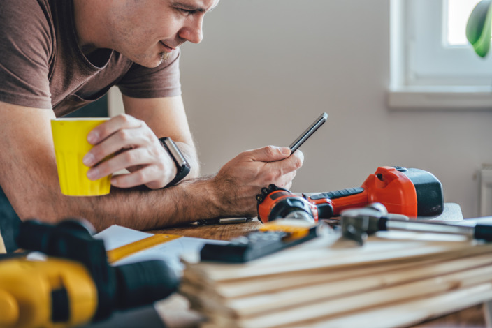 Handwerker schaut auf sein Handy und trinkt Kaffee.