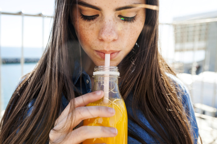 junge Frau trinkt ein isotonisches Getränk mit einem Strohhalm aus einer Flasche