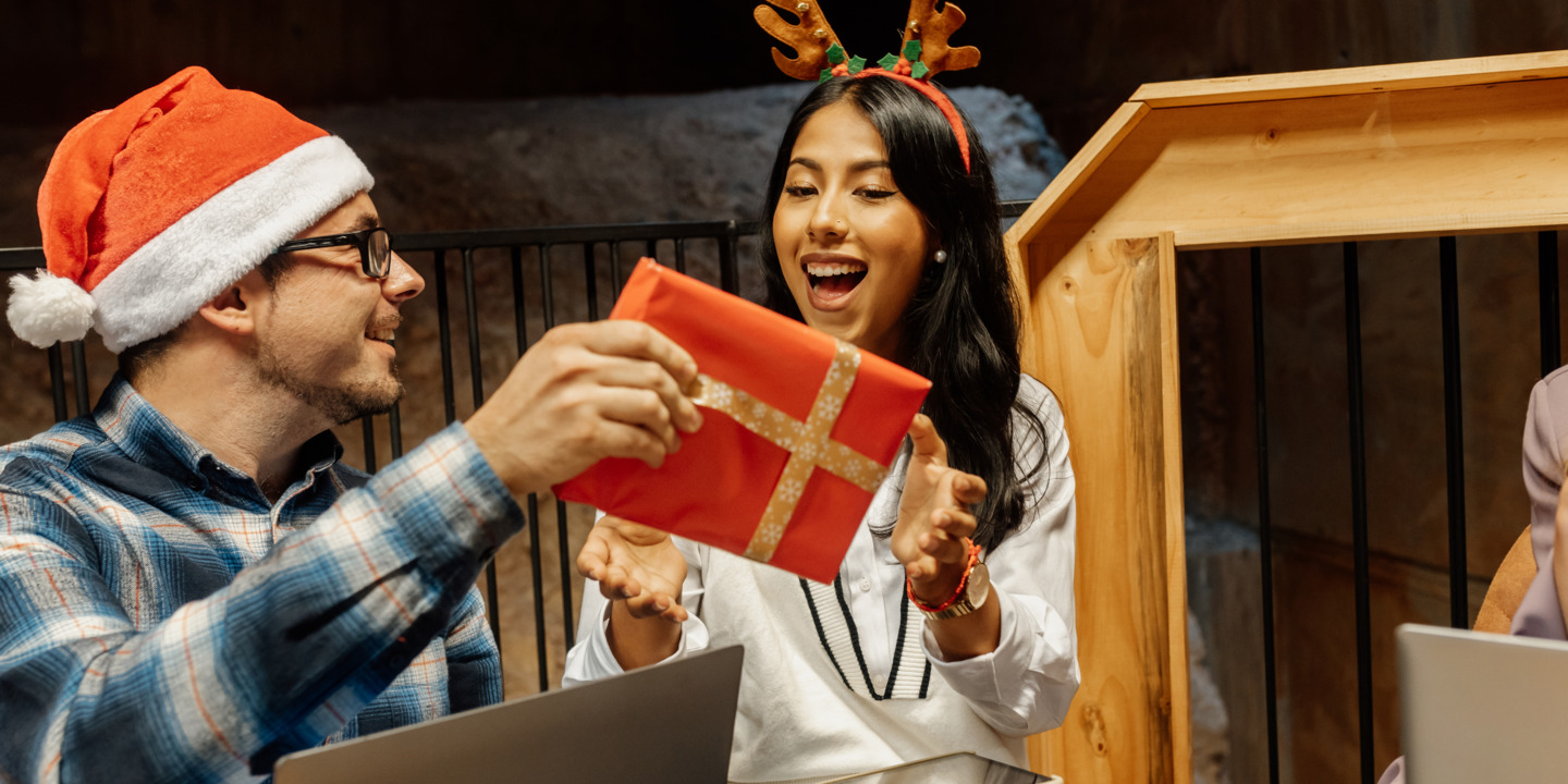 Kollege übergibt ein verpacktes Weihnachtsgeschenk an seine Kollegin 