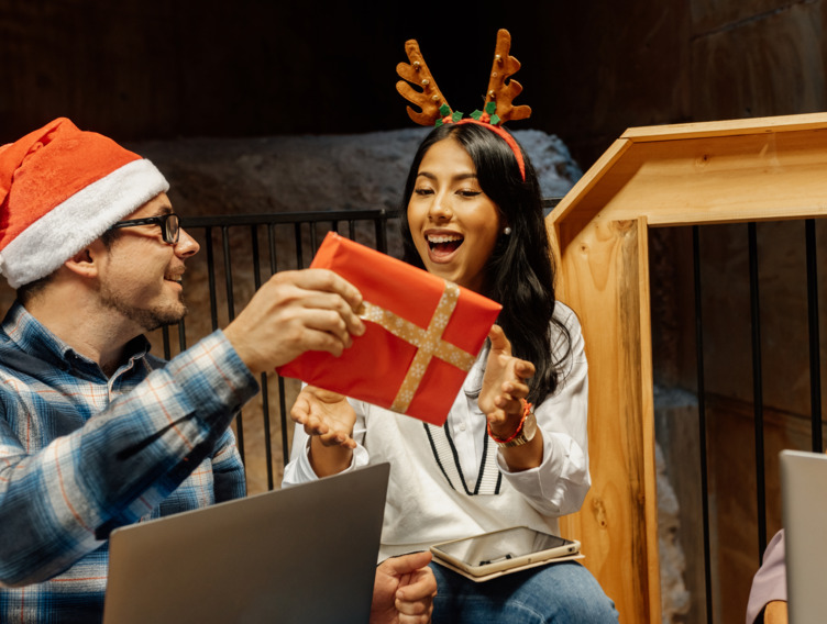 Kollege übergibt ein verpacktes Weihnachtsgeschenk an seine Kollegin