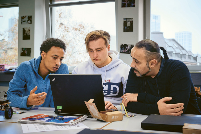 Zwei Auszubildene sitzen mit ihrem Lehrer zusammen am Laptop