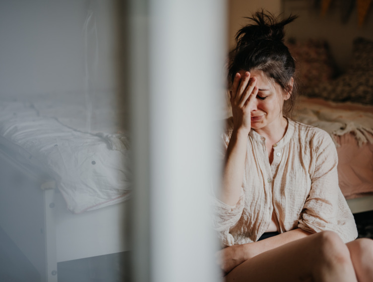 Eine weinende Frau, die auf ihrem Schlafzimmerboden sitzt