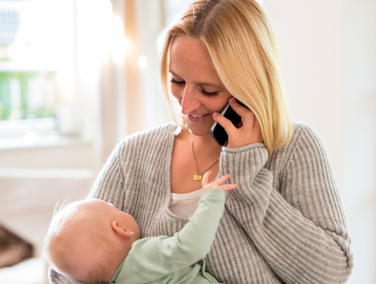 Telefonierende Frau trägt Baby auf dem Arm