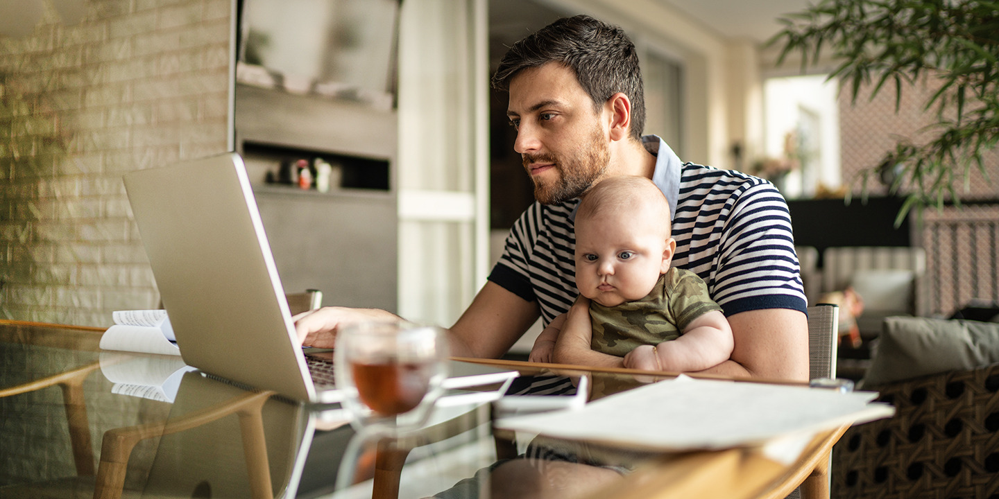 Mann sitzt mit seinem Baby auf dem Arm am Laptop