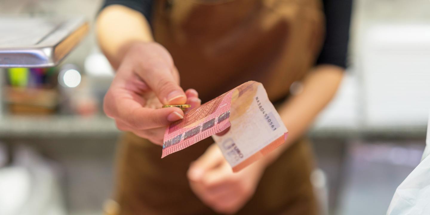 Person hält Geldschein und Münze in der Hand