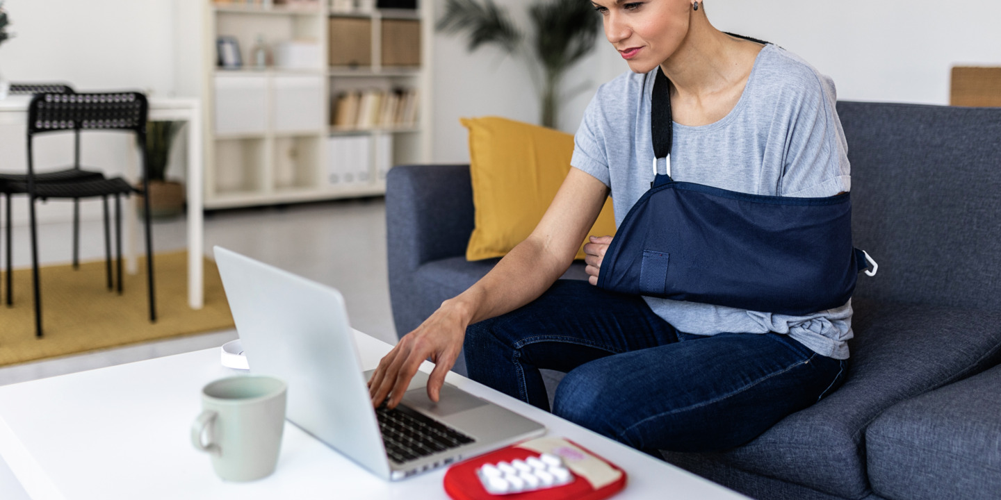 Person mit verletztem Arm sitzt am Laptop und tippt