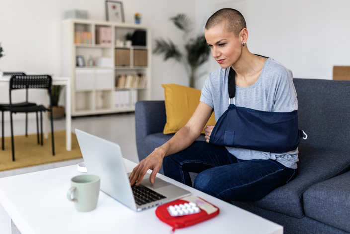 Person mit verletztem Arm sitzt am Laptop und tippt