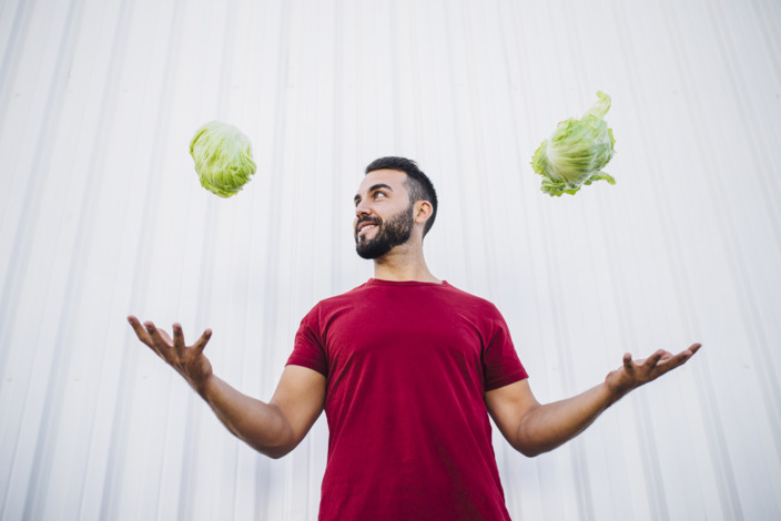 Sportlicher Mann wirft in jeder Hand einen Salat in die Luft