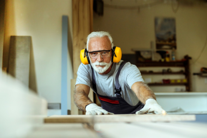 Ein älterer Mann schneidet Holz in einer Werkstatt. 