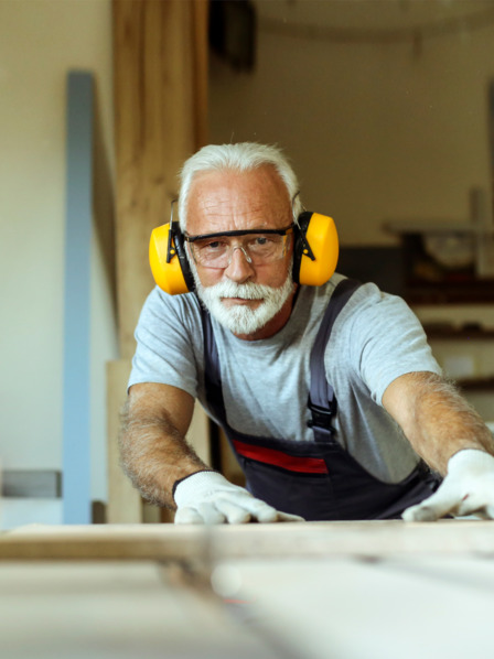 Ein älterer Mann schneidet Holz in einer Werkstatt. 