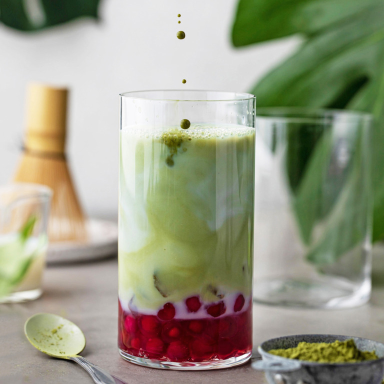 Ein Glas gefüllt mit grünem Tee, Kokosmilch und Früchten.