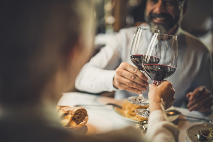 Paar stößt beim Restaurantbesuch mit zwei Gläsern Rotwein an