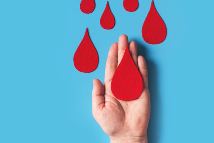 Bluttropfen aus rotem Filz auf Hand vor blauem Hintergrund