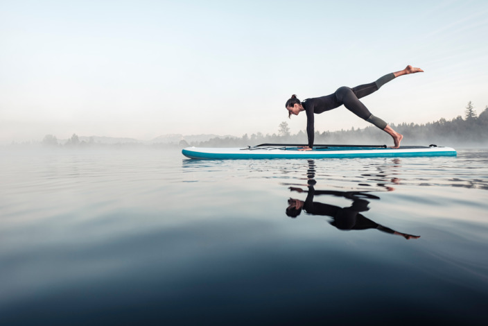 Frau macht Gymnastik-Pose auf einem Surfbrett auf dem Wasser