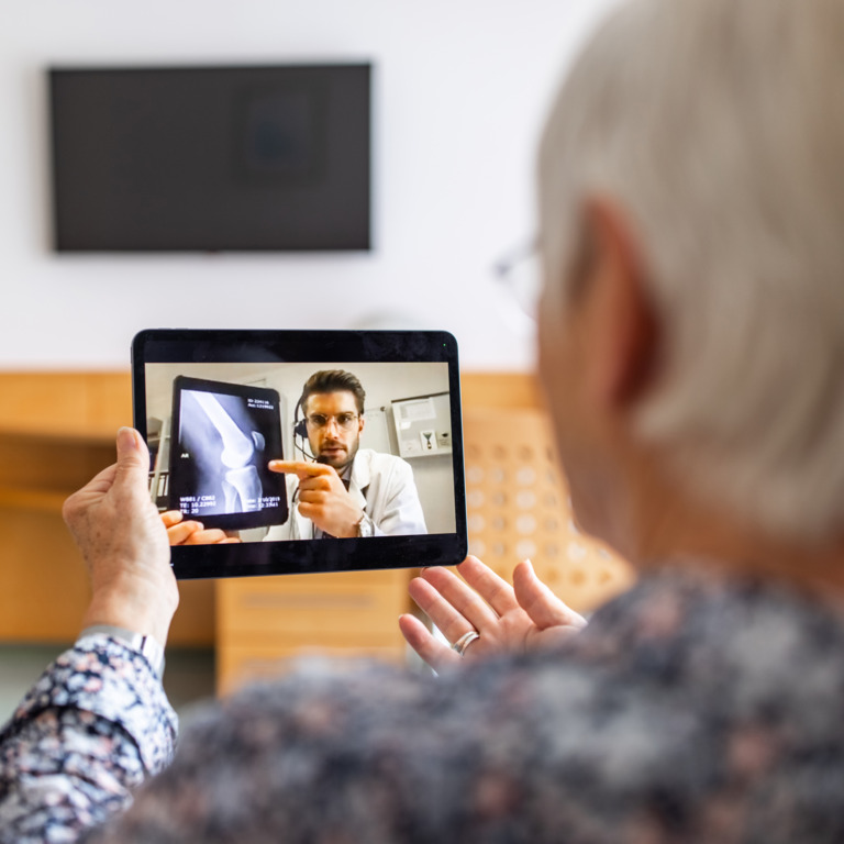 Frau sitzt vor einem Tablet in einer Videosprechstunde mit einem Arzt, der ihr Röntgenbilder erklärt