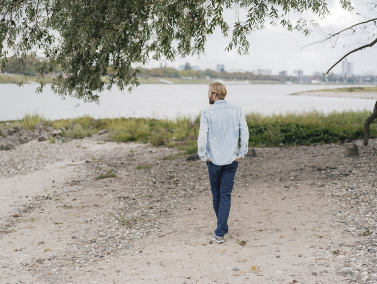 junger Mann geht gedankenversunken am Ufer eines Flusses entlang