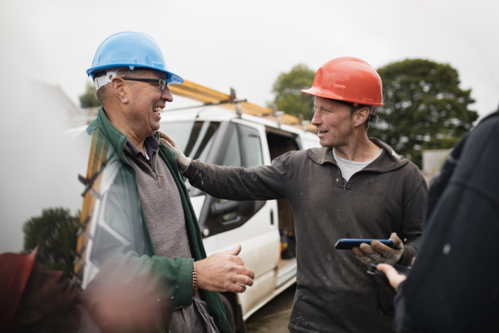 Zwei Handwerker stehen vor ihrem Lieferwagen und lachen miteinander