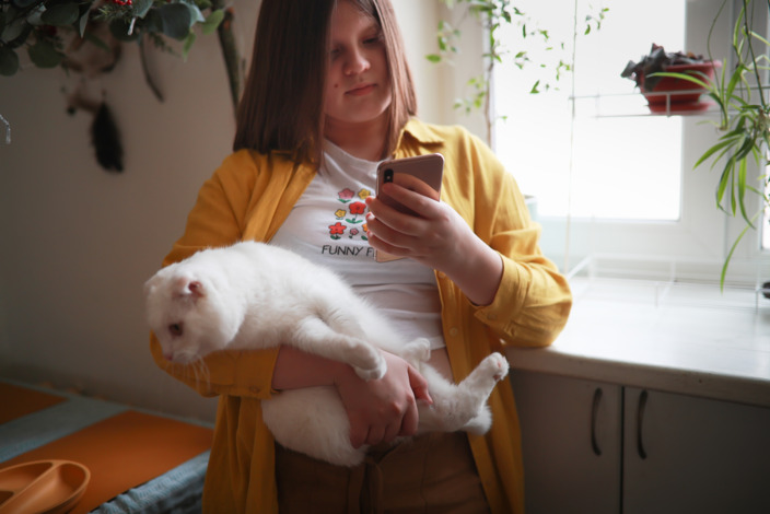 Ein übergewichtiges Kind hält eine Katze auf dem Arm und schaut auf ein Smartphone – Symbolbild für Übergewicht bei Kindern