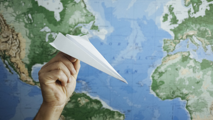 Hand hält ein Papierflugzeug vor einen Globus